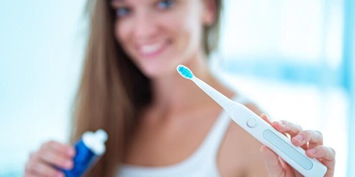 Happy healthy smiling woman with ultrasonic electric brush in ba